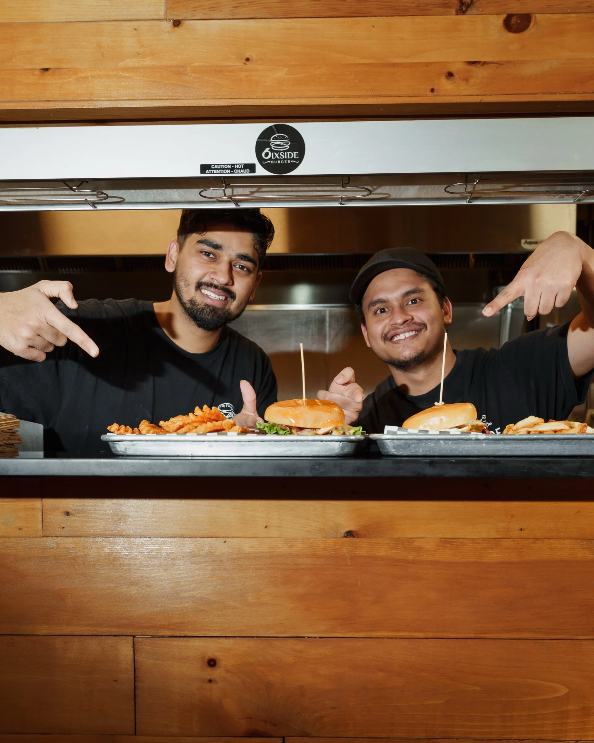 Two Sixside cooks pointing at burgers on the pass